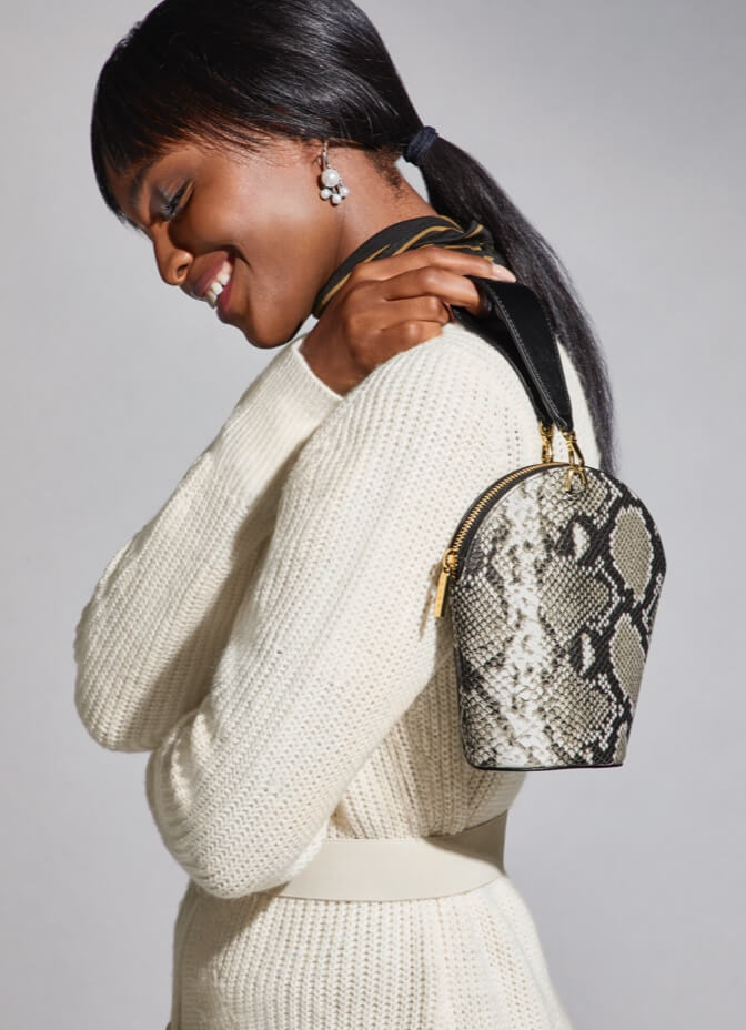 Model Wearing the Slinky Turtleneck in Camel and Black, Book Club Cardigan in Ivory, Clutch Earrings in Antique Silver, and Serpent Mini Bag in Snakeskin Print.