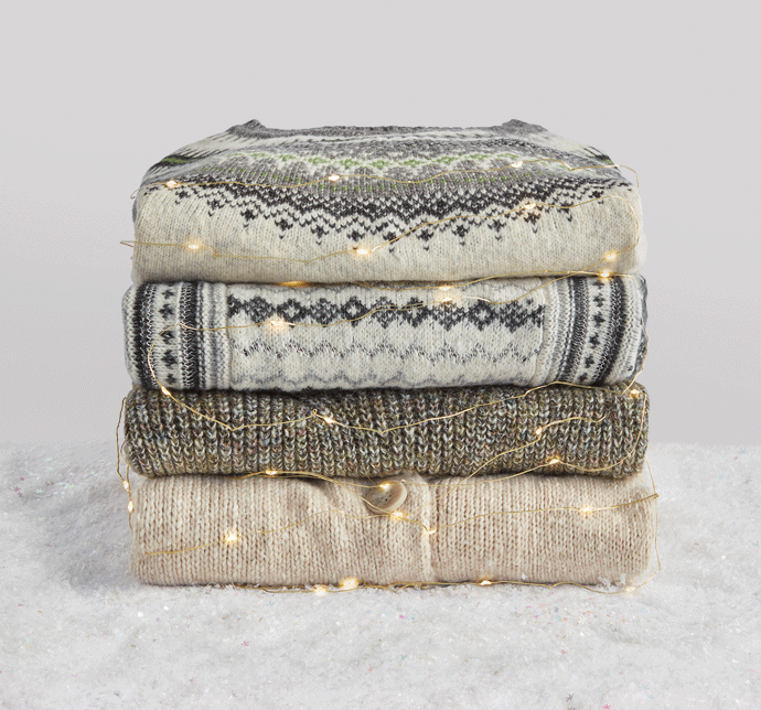 sweater stack wrapped in lights including Shetland Pullover in Fair Isle, Chalet Pullover in Gray and Ivory, The Tunic Dress in Artichoke, and Steady Cardigan in Wheat.